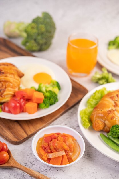 Завтрак, состоящий из хлеба, яичницы, брокколи, моркови, помидоров и салата на белой тарелке.