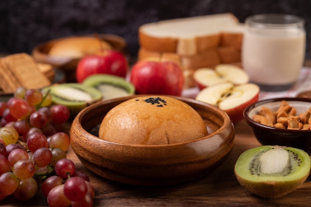 Breakfast consists of bread, apples, grapes and kiwi on a wooden table