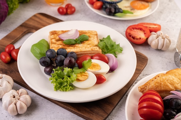 Завтрак состоит из хлеба, вареных яиц, салата из черного винограда, помидоров и нарезанного лука.