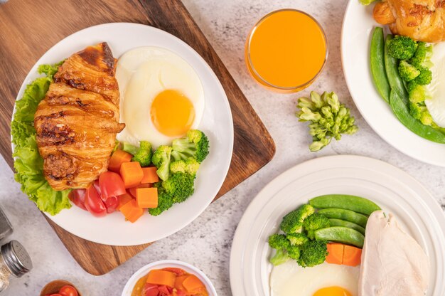 Breakfast consists of chicken, fried eggs, broccoli, carrots, tomatoes and lettuce on a white plate.