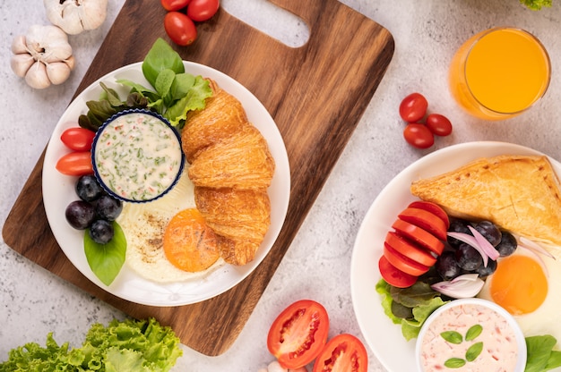 Breakfast consists of croissant, fried egg, salad dressing, black grapes, and tomatoes.