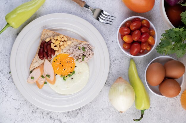 아침 식사는 튀긴 계란, 소시지, 다진 돼지 고기, 빵, 팥 및 흰 접시에 콩으로 구성됩니다.