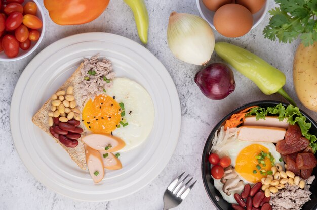 Breakfast consists of fried eggs, sausage, minced pork, bread, red beans and soy on a white plate.