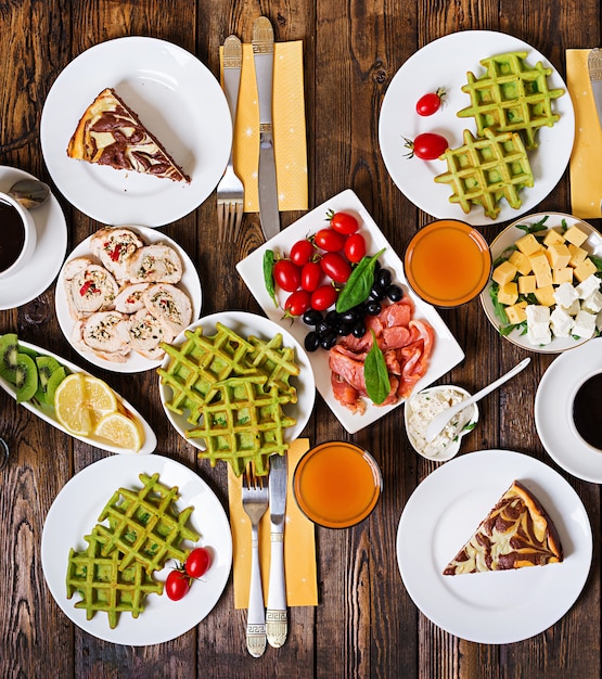 Free photo breakfast food table. festive brunch set, meal variety with spinach waffles, salmon, cheese, olives, chicken rolls and cheesecake. top view. flat lay