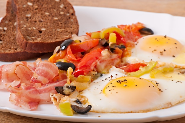 Free photo breakfast - fried eggs with bacon, tomatoes, olives and slices of cheese