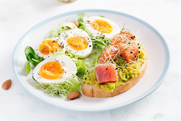 Breakfast. Healthy open sandwich on  toast with avocado and salmon, boiled eggs, herbs, chia seeds on white plate  with copy space. Healthy protein food.