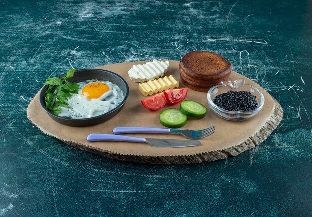 Breakfast menu on a wooden board with fried egg, caviar and pancakes. High quality photo