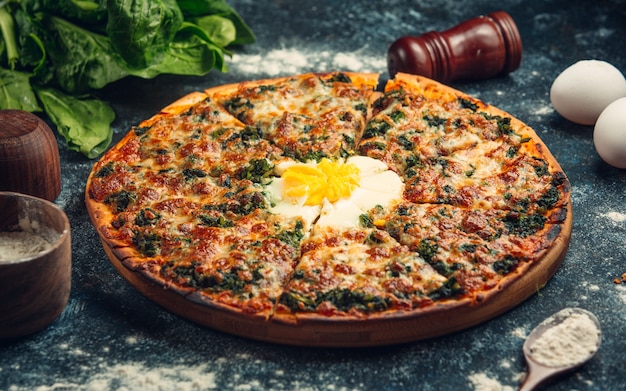 breakfast pizza with pesto sauce and sunny side up egg in the middle