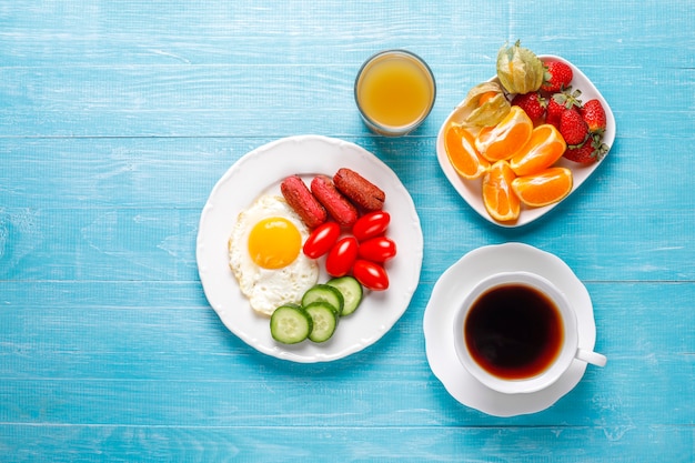 칵테일 소시지, 계란 후라이, 체리 토마토, 과자, 과일, 복숭아 주스 한 잔이 포함 된 조식 접시입니다.