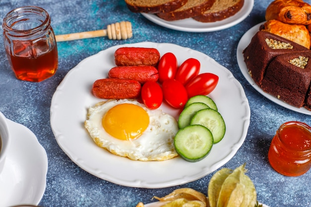 A breakfast plate containing cocktail sausages,fried eggs,cherry tomatoes,sweets,fruits and a glass of peach juice.