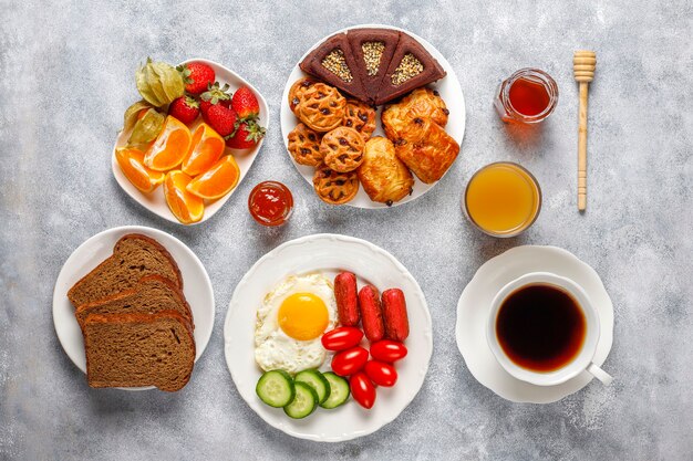 A breakfast plate containing cocktail sausages,fried eggs,cherry tomatoes,sweets,fruits and a glass of peach juice.