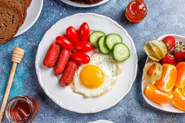 칵테일 소시지, 계란 후라이, 체리 토마토, 과자, 과일, 복숭아 주스 한 잔이 포함 된 조식 접시입니다.