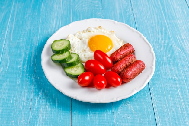 A breakfast plate containing cocktail sausages,fried eggs,cherry tomatoes,sweets,fruits and a glass of peach juice.