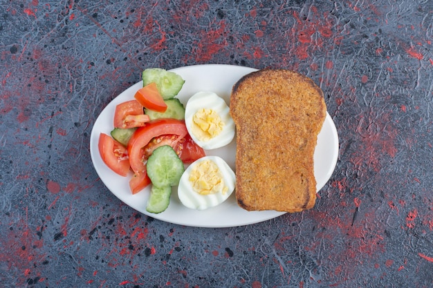 Breakfast plate with egg, cucumber, tomato and bread slices. 