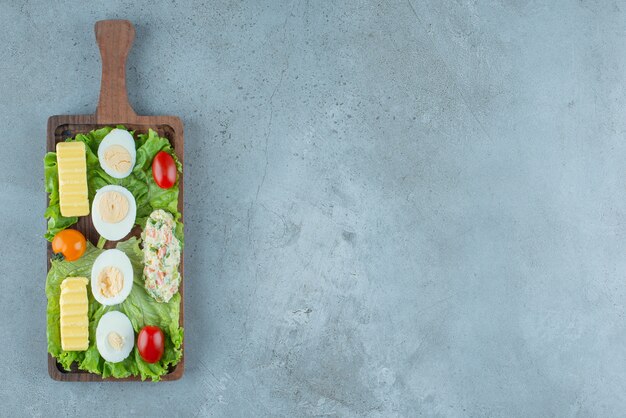 Breakfast set on a wooden tray with vegetables, boiled eggs, butter and a salad serving, on marble background. High quality photo