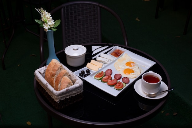 Breakfast tray with fried eggs, sausages, cheese, jam, butter, bread and a cup of tea.