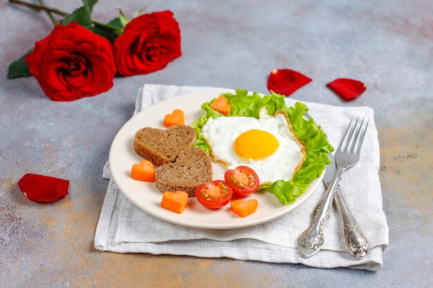 Завтрак в День святого Валентина - яичница и хлеб в форме сердца и свежие овощи.