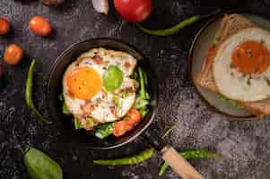 Бесплатное фото Завтрак с яичницей, колбасой и ветчиной на сковороде с помидорами. чили и базилик