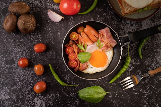 Breakfast with fried eggs, sausage, and ham in a pan with tomatoes. Chili and basil.