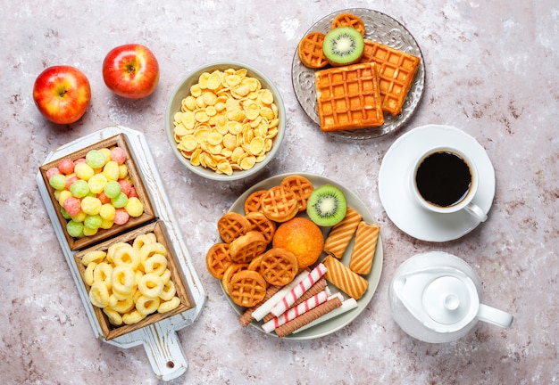 Завтрак с различными сладостями, вафлями, кукурузными хлопьями и чашкой кофе, вид сверху