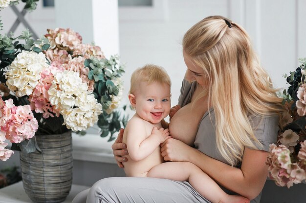 Breastfeeding baby sitting on laps in studio room decorated with flowers. 