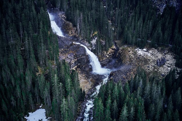 Breathtaking high angle shot of a waterfall on a rock surrounded by a forest of tall spruces