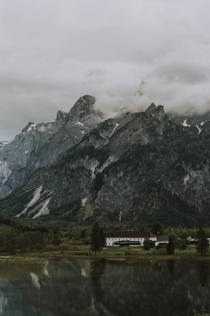 Breathtaking shot of the brown and white house near the lake and mountains under a cloudy sky