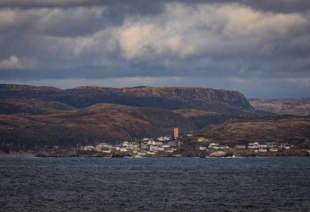 Free photo breathtaking shot of a deep blue ocean and a small town below a mountain range on a cloudy day