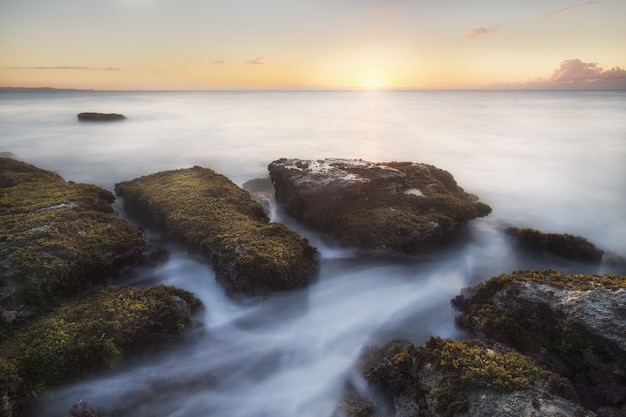 Breathtaking shot of huge stones in the ocean with the foamy water passing through them