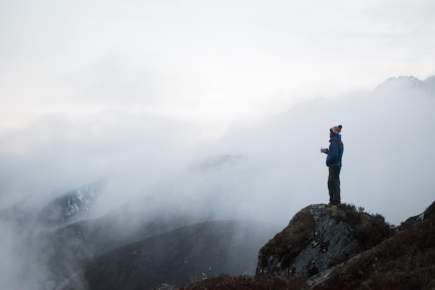 Захватывающий снимок мужчины, стоящего на вершине большой скалы в окружении туманных гор.