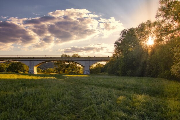 Breathtaking sunset over a green forest with a long bridge in the middle