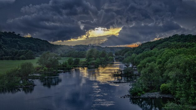 Breathtaking susnet at a river in the middle of a green forest under the dark sky