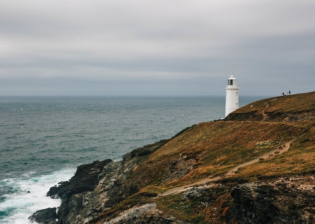 Breathtaking view of a lighthouse on a grass-covered hill by the ocean on a cloudy day