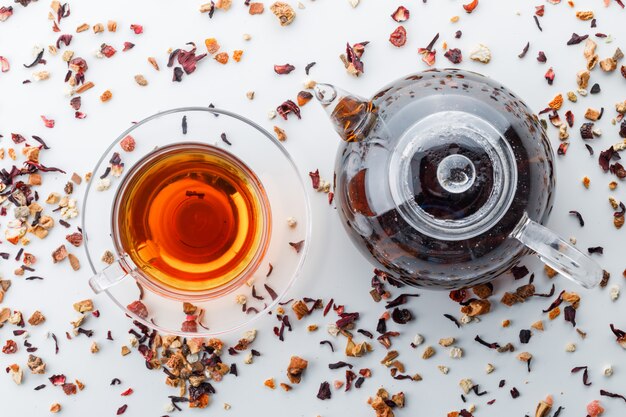 Brewed tea in teapot and cup with mixed dried herbs top view on a white surface