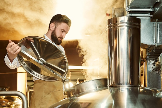 Free photo brewer looking in metallic brew kettle with steam