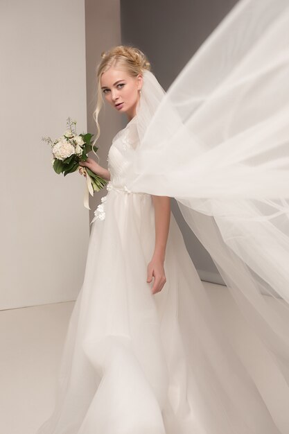 Bride in beautiful dress standing indoors in white studio interior like at home. Trendy wedding style shot. Young attractive caucasian model like a bride tender looking.