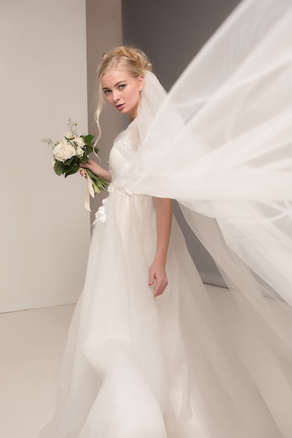 家のような白いスタジオインテリアで室内で立っている美しいドレスの花嫁。トレンディなウェディングスタイルのショット。探している花嫁の入札のような若い魅力的な白人モデル。