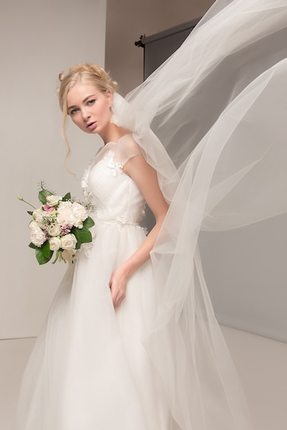 Bride in beautiful dress standing indoors in white studio interior like at home.