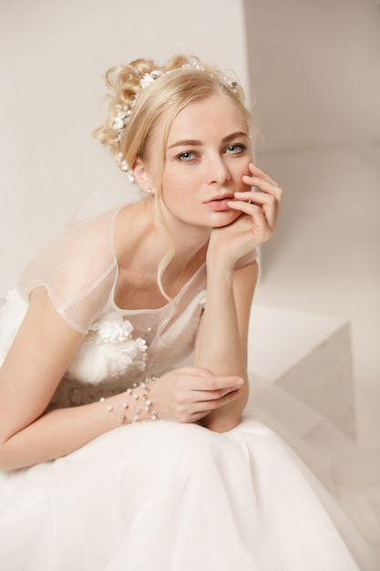 Bride in beautiful dress standing indoors in white studio interior like at home.