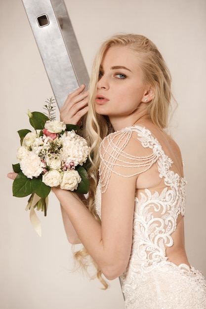 Bride in beautiful dress standing indoors in white studio interior like at home.