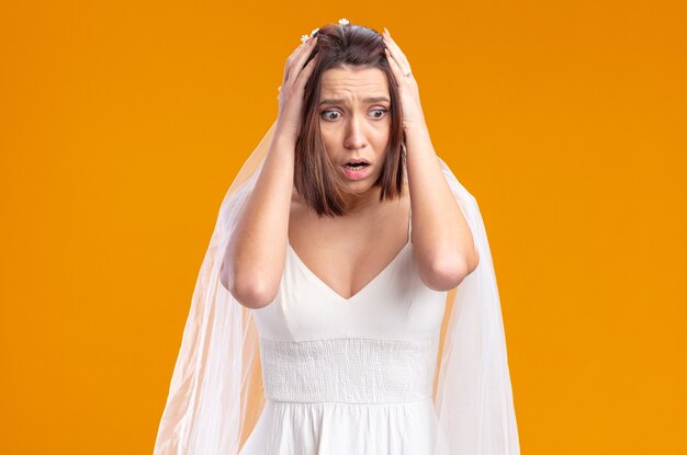 Bride in beautiful wedding dress looking aside being shocked with hands on her head