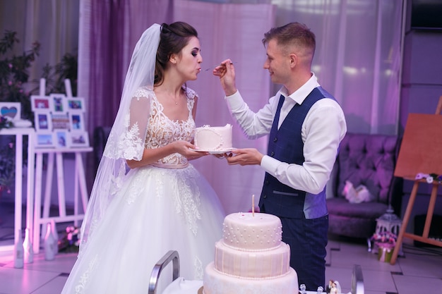 Bride and groom eating beautiful   wedding cake with cream on the party with spoon. wedding couple bride and groom cut the white festive cake . wedding day