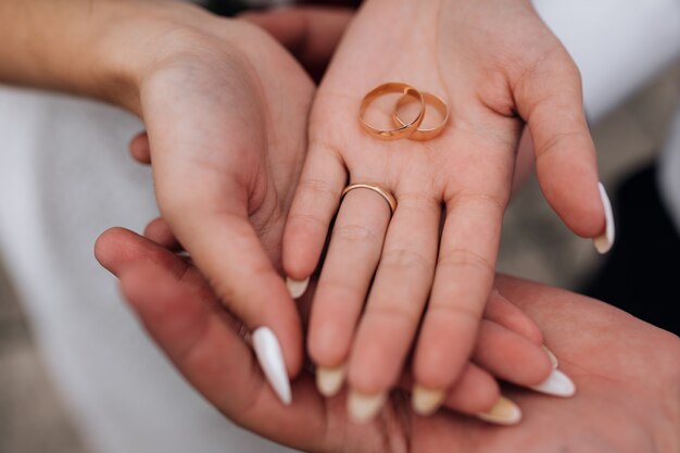 Bride and groom hold classy golden wedding rings in their arms