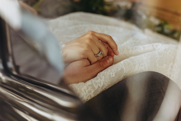 Foto gratuita la sposa e lo sposo si tengono le mani seduti all'interno dell'auto