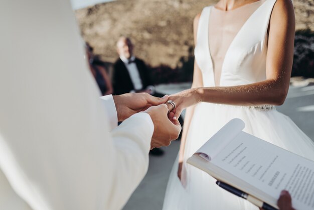 Жених и невеста в легкой летней одежде держат друг друга за руки во время церемонии
