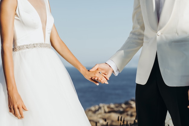 Bride and groom in light summer clothes hold each other hands during the ceremony