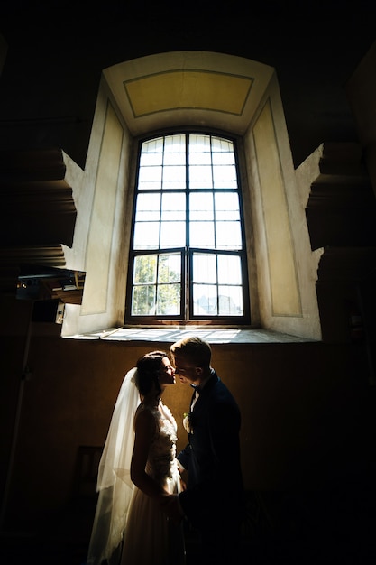 大きな窓の背景にポーズをとる新郎新婦