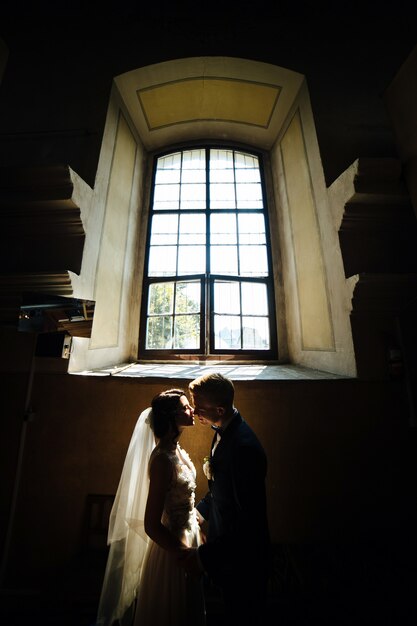 Bride and groom posing on the background of a large window
