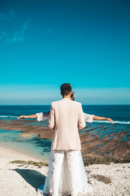 bride and groom posing on the cliff behind blue sky and sea