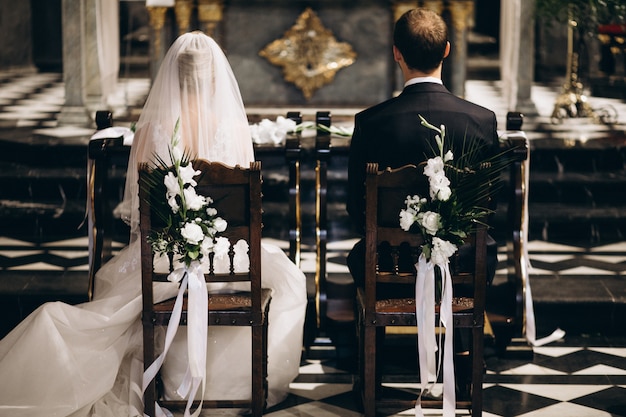 Bride and groom sitting on chairs on their wedding day, from the back